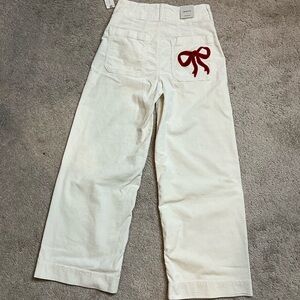 Anthropologie Cream Woman Bottoms with Red Bow on back right pocket.